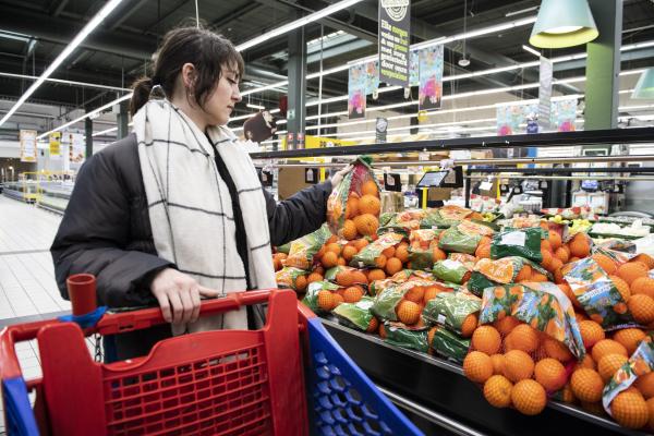 Woman handling bag of oranges from supermarket stack