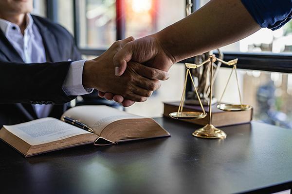 Two people shaking hands next to the scales of justice