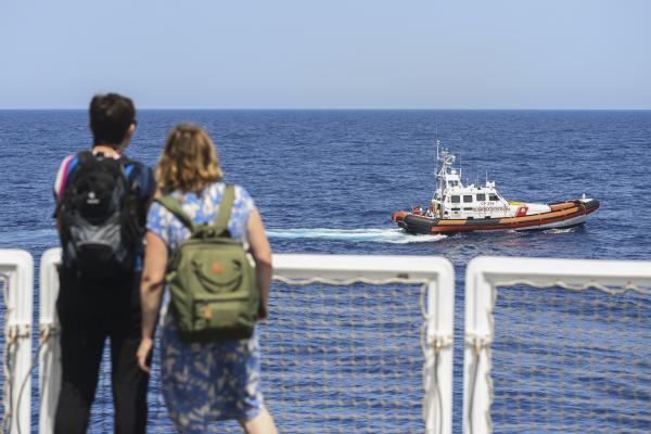 Man and woman stare out to sea at search and rescue boat going past, Sicily