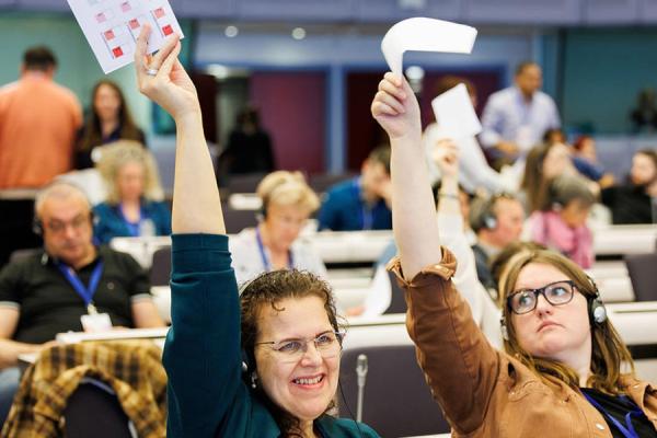 Two women with their left hands raised in an Erasmus + Evaluation Democracy meeting