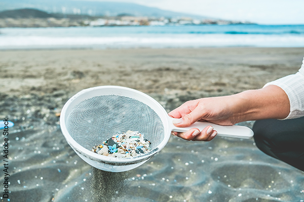 Person's arm holding out a sieve full of plastic pellets on a beach