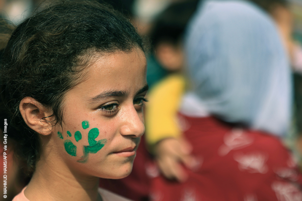 A Palestinian child who fled her home due to Israeli strikes, shows off her painted cheek with the word 'Gaza'
