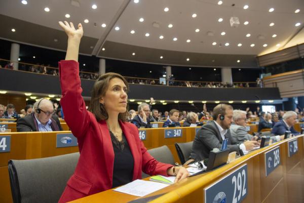 Woman in red jacket raising her hand at her desk in the plenary voting session at the European Parliament - 9 November 2023