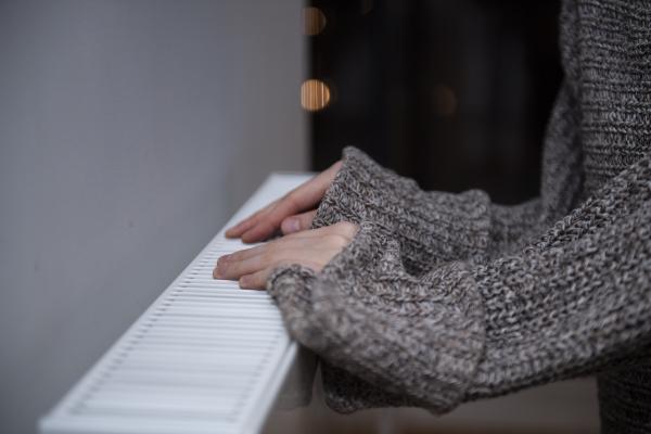 A woman wearing thick, long-sleeved clothes puts her hands on the radiator