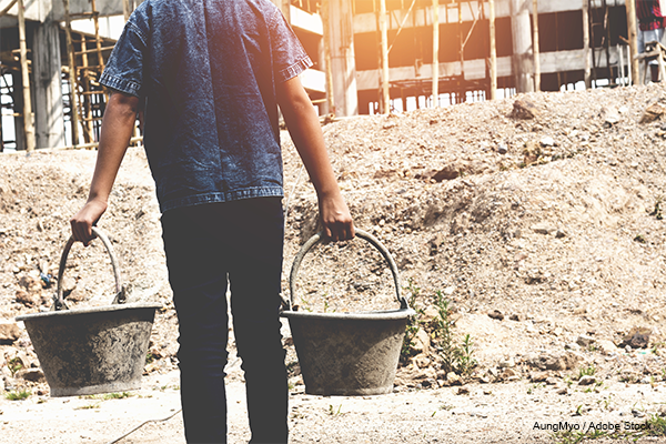 Child carrying two buckets on a construction site