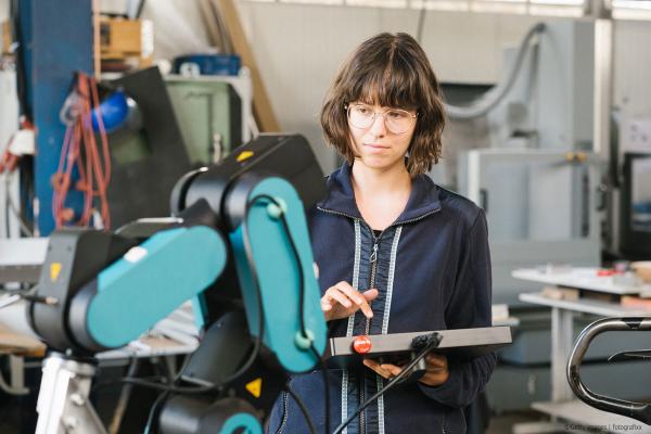 female technician programs a robot arm with a digital tablet