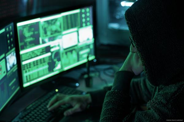 Hooded man stares in dark at computer monitors
