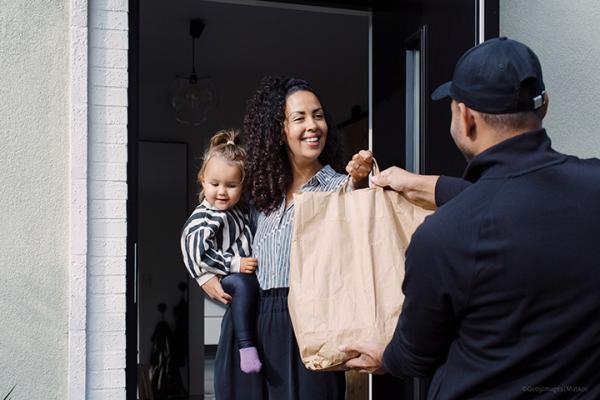 A woman holding a child receives a package at her front door