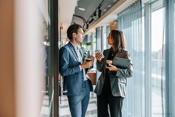 Female entrepreneur standing with male colleague and discussing in office corridor