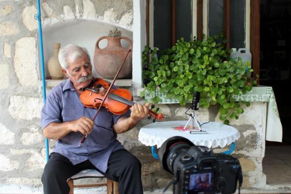 Elderly Cypriot man sitting outside a house playing a fiddle
