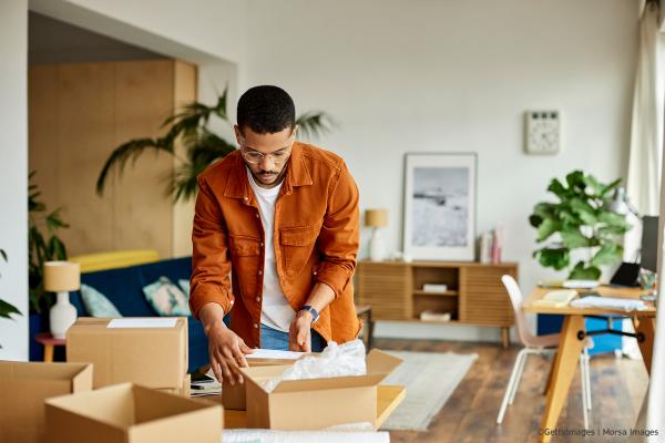 Young businessman packing cardboard box at table in apartment. Male professional is working at home office. He is in the living room.