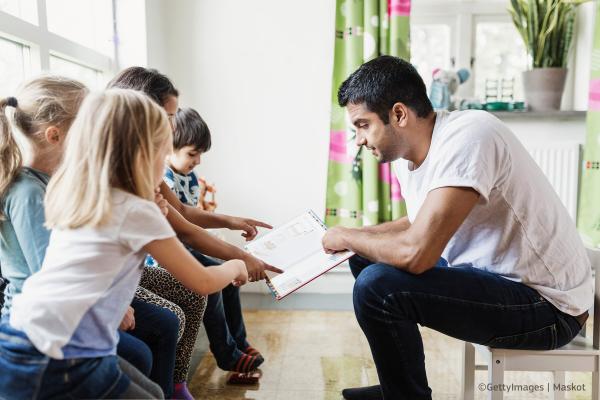Side view of sitting teacher talking to his small pupils in a classroom