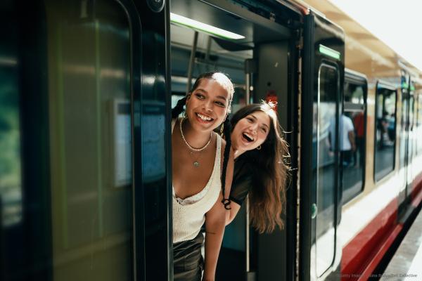 Two young women look out of an open door of a train